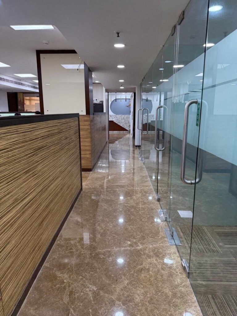 Modern corporate office corridor with marble flooring, glass partitions, and wood finishes, designed by Shree Spaace Solution for MMG Agarwal Group.